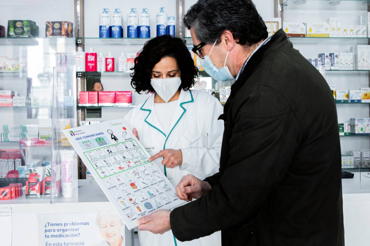  Irene Pérez, de la Farmacia Central de Marchena (Sevilla), muestra a un hombre los pictogramas que se usan en la comunicación con personas con trastorno del espectro autista.